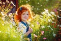 Closeup beautiful portrait ginger curly little girl in the blossoming flower garden