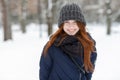 Closeup beautiful winter portrait of young adorable smiling redhead woman in cute knitted hat winter snowy park Royalty Free Stock Photo