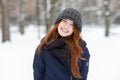 Closeup beautiful winter portrait of young adorable smiling redhead woman in cute knitted hat winter snowy park Royalty Free Stock Photo