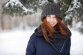 Closeup beautiful winter portrait of young adorable smiling redhead woman in cute knitted hat winter snowy park Royalty Free Stock Photo