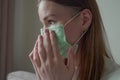 Closeup of a beautiful young girl with long red hair straightens a medical mask on her face. Orvi, coronovirus, influenza.