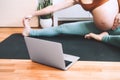 Closeup belly of pregnant woman practicing yoga online with laptop