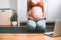 Closeup belly of pregnant woman practicing yoga online with laptop
