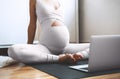 Closeup belly of pregnant woman practicing yoga online with laptop