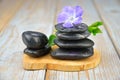 Closeup of black balancing rocks with a purple flower on a wooden surface Royalty Free Stock Photo