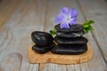 Closeup of black balancing rocks with a purple flower on a wooden surface Royalty Free Stock Photo