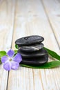 Closeup of black balancing rocks with a purple flower on a wooden surface Royalty Free Stock Photo