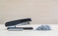 Closeup black stapler with blurred pile of used staples and new staples , office equipment on blurred wood desk and wall in offic