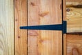 Closeup of black wrought iron hand forged t-hinge on waney edge wooden shed door.