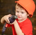 Closeup blond boy holding big drill. Little builder on construction site. Cute kid in orange protective helmet isolated