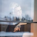Closeup of a blonde Caucasian female sitting behind the window looking outside with a pensive glance Royalty Free Stock Photo