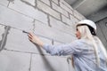 Closeup blonde girl designer foreman in white construction helmet measures the grey wall of sibit by tape measure in house under