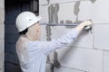 Closeup blonde girl designer foreman in white construction helmet measures the grey wall of sibit by tape measure in house under