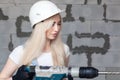 Closeup blonde girl foreman in white construction helmet holding professional perforator, drill in house under construction. Royalty Free Stock Photo
