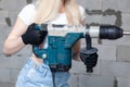 Closeup blonde girl foreman in white construction helmet holding professional perforator, drill in house under construction. Royalty Free Stock Photo