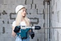 Closeup blonde girl foreman in white construction helmet holding professional perforator, drill in house under construction. Royalty Free Stock Photo