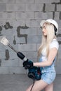 Closeup blonde girl foreman in white construction helmet holding professional perforator, drill in house under construction. Royalty Free Stock Photo