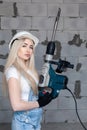 Closeup blonde girl foreman in white construction helmet holding professional perforator, drill in house under construction. Royalty Free Stock Photo