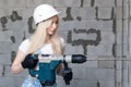 Closeup blonde girl foreman in white construction helmet holding professional perforator, drill in house under construction. Royalty Free Stock Photo