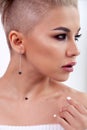 Closeup blonde model with bright make-up, bare shoulders and short hair with shaved temples in modern round silver jewelry