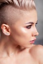 Closeup blonde model with bright make-up, bare shoulders and short hair with shaved temples in modern round silver jewelry