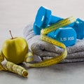 Closeup of blue dumbbells, apple, grey towel and measuring tape