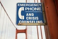 Closeup of a blue [Emergency Phone And Crisis Counseling] sign on a bridge with a blurry background Royalty Free Stock Photo