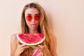 Closeup of bohemian fashion beautiful young Caucasian blonde woman with red sunglasses holding a watermelon slice. Attractive girl Royalty Free Stock Photo