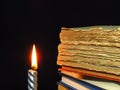 Closeup of books pile and a burning candle. A pile of old books is pictured against dark black background. Royalty Free Stock Photo