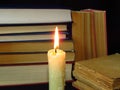 Old books stacked in a pile and a burning candle. Education, knowledge, reading habits, paper, library, light, flame, mystery.