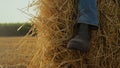 Closeup boot hay stack at wheat stubble field. Farmer resting at straw bale