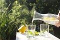 Woman poring water with lemon into glass.Refremnet time in the garden.Sunny and hot day in the garden