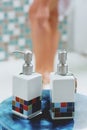 Closeup bottle of cream and applying moisturizing hand cream. Beautiful female legs with cream in shower. Royalty Free Stock Photo