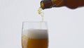 Closeup bottle pouring beer into glass at white background. Lager drink flowing