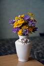 Closeup of a bouquet of white, yellow and purple wild meadow flowers in a white vase on the edge of a table Royalty Free Stock Photo