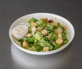 Closeup of a bowl of Caesar salad with sauce on a gray table Royalty Free Stock Photo