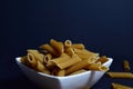 Closeup of bowl of raw whole wheat Penne pasta on dark blue background Royalty Free Stock Photo