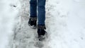 Closeup of boy in snowboots walking over covered snowdrifts and road covered with snow and ice.