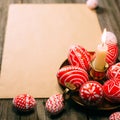 Closeup brass candlestick with Easter red eggs with folk white pattern stand on paper on rustic table. Ukrainian traditional eggs