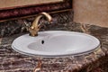 Closeup of a brass faucet with hot and cold handles on a white lavatory sink in a restroom