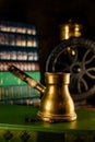 Closeup brass turk with beans beside and coffee grinder on background. Atmosphere of old library with old books around on dark Royalty Free Stock Photo