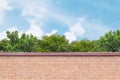 Closeup brick pattern at the brown brick wall of fence with green tree and blue sky with cloud textured background Royalty Free Stock Photo