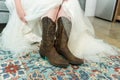 Closeup of the bride wearing a white wedding dress with cowboy boots in her dressing ro