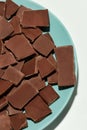 Closeup of broken, crushed dark chocolate bars stack on a plate isolated over white background