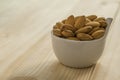 Closeup of brown fresh almonds seed in white bowl on wooden table