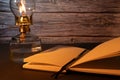 Closeup of a burning old antique hurricane oil lamp with open book on wooden table