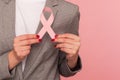 Closeup of business person in elegant suit jacket holding pink ribbon, warning of breast cancer risk and society awareness