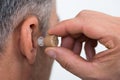 Closeup Of Businessman Inserting Hearing Aid In Ear