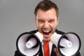 Closeup of businessman screaming in two megaphones on grey background.