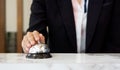 Closeup of a businesswoman hand ringing silver service bell on hotel reception desk